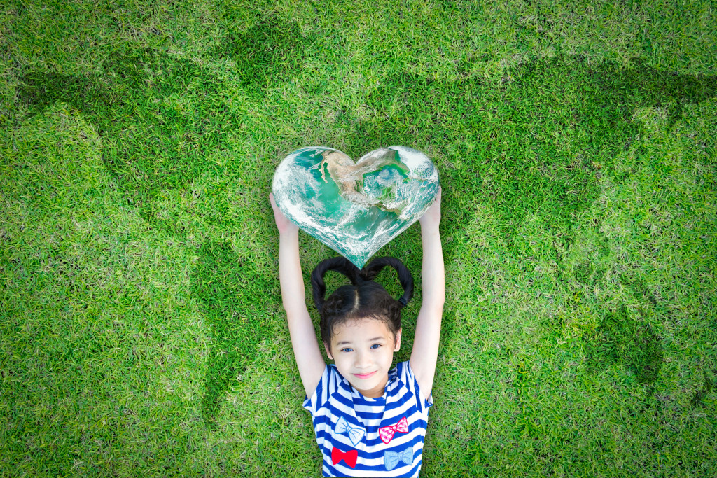 Smiling happy healthy child kid holding heart shaped green globe on world map grass background