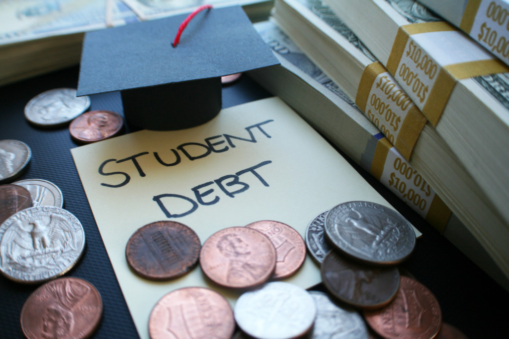 Student debt written on a note with coins, a paper graduation hat, and paper money